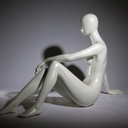 Faceless female mannequin. White, matte with faceless head. Seated